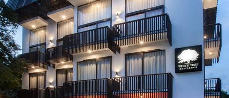A multi-story hotel with balconies, a covered outdoor seating area, and a sign indicating "White Tree Residence."