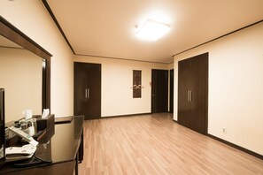 Quarto de hotel com piso de madeira, uma escrivaninha com telefone e dois armários.