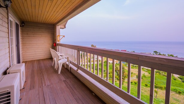A wooden balcony with a view of the sea, a chair, and a fire extinguisher. - Daea Ulleung Resort (Ulleung)