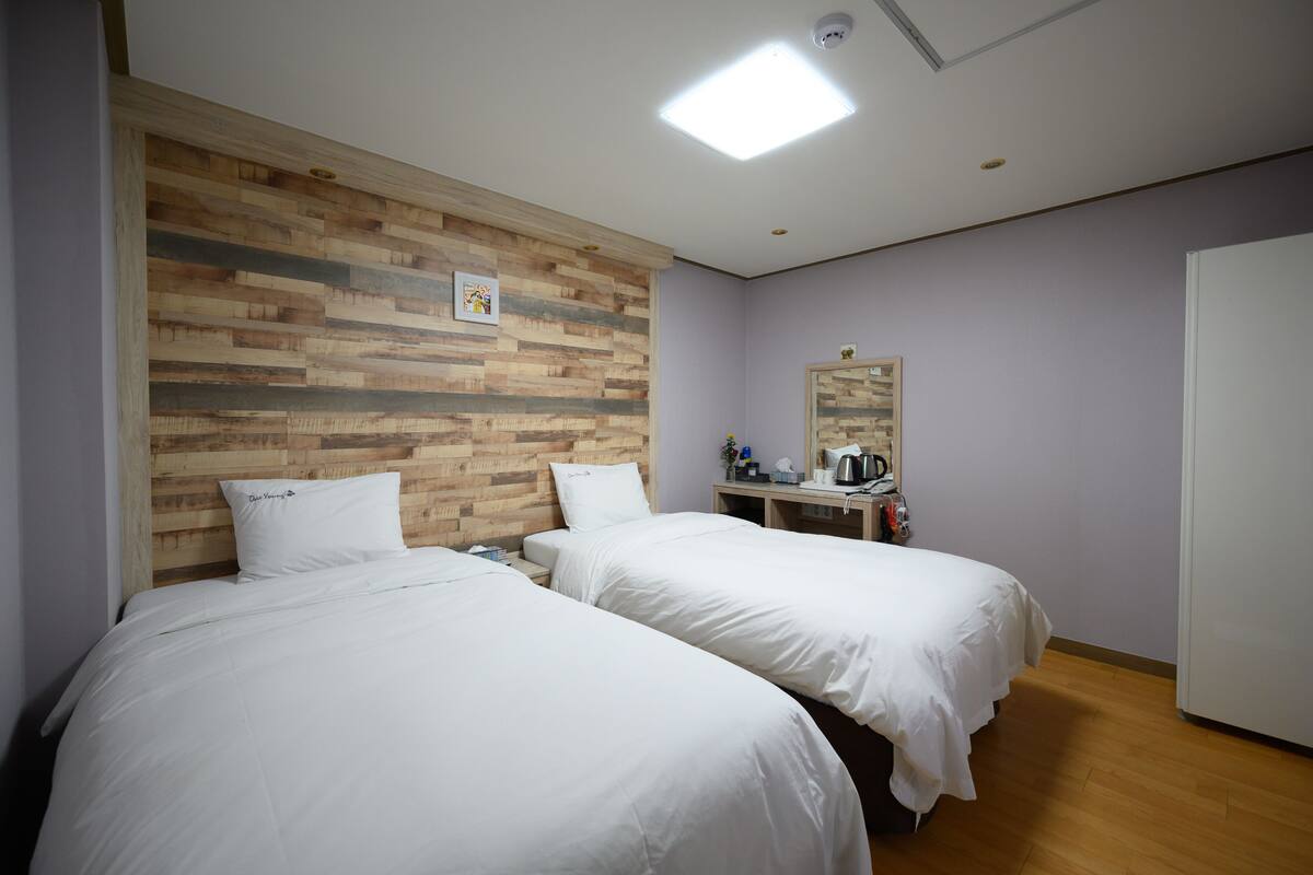 Une chambre d’hôtel avec deux lits, une tête de lit en bois, un bureau avec un miroir et une armoire blanche.