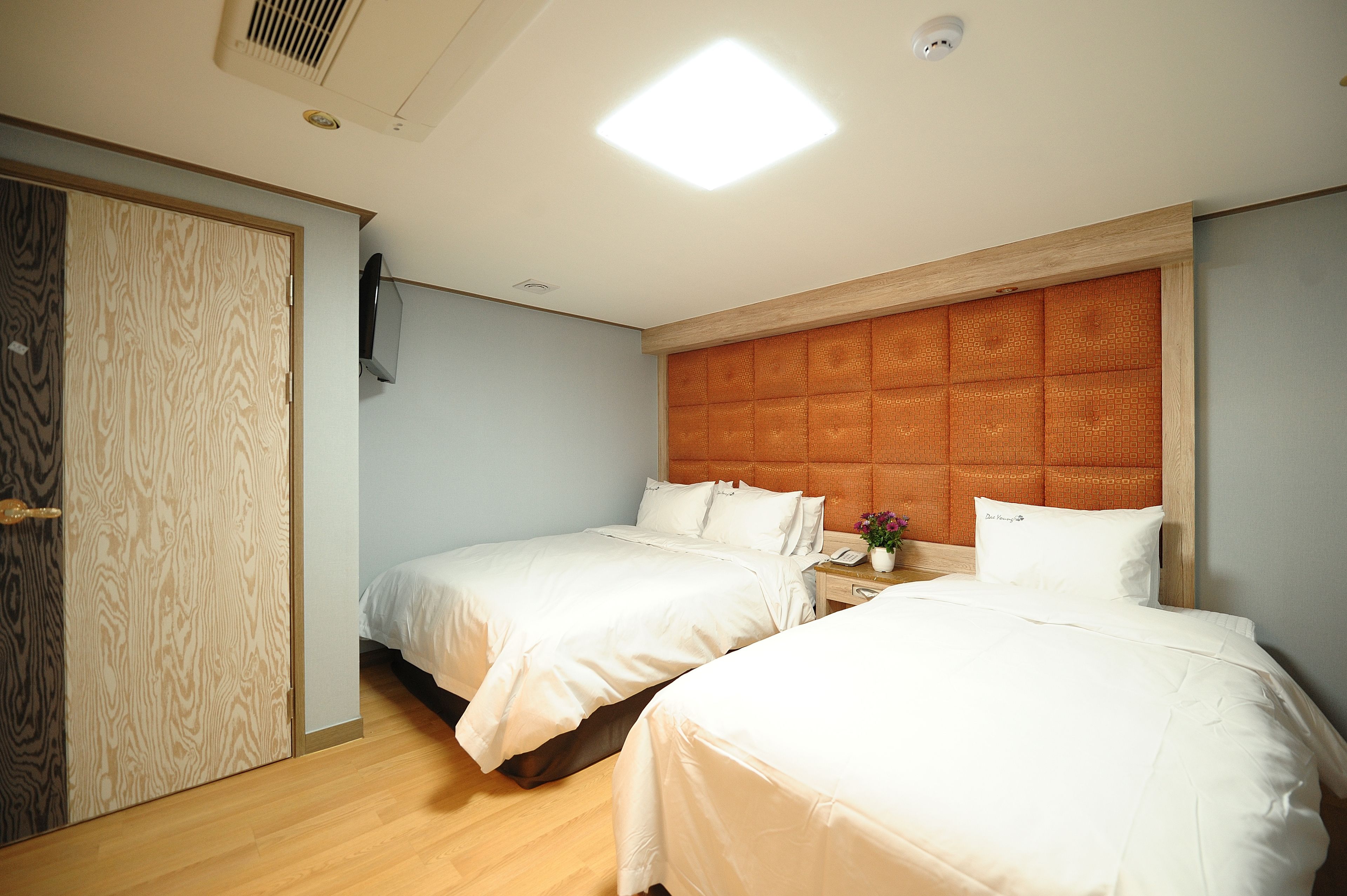Habitación de hotel con dos camas, un armario de madera, un cabecero con motivo geométrico y una lámpara en el techo.
