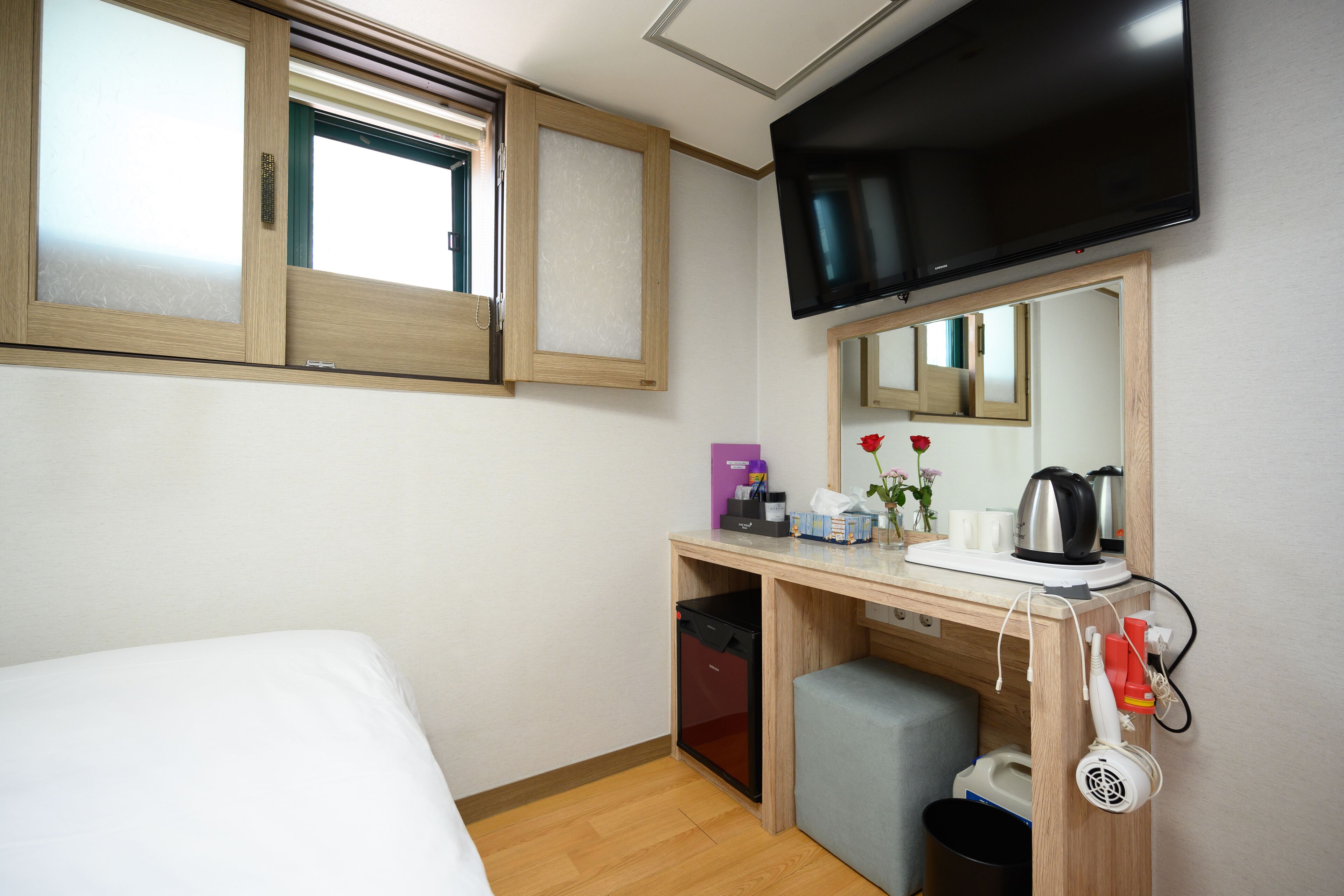 Habitación de hotel con cama, escritorio con espejo, televisor y pequeña zona de kitchenette.