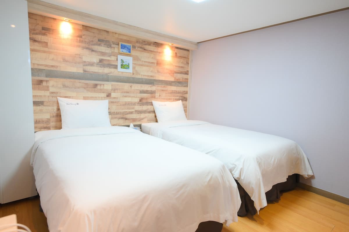 Une chambre d’hôtel avec deux lits simples, une tête de lit en bois et un luminaire fixé au mur.