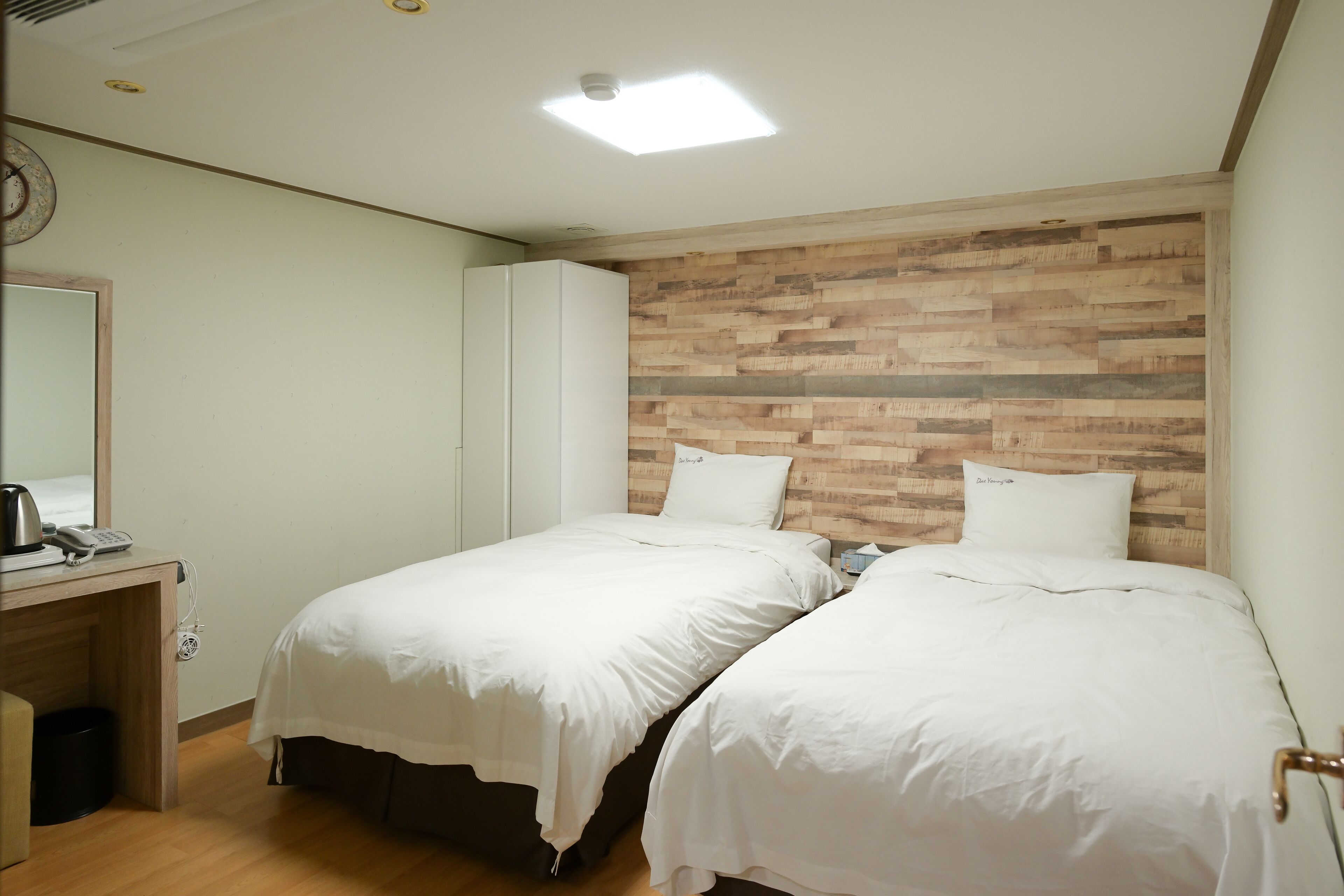 Une chambre d’hôtel avec deux lits, une tête de lit en bois, un bureau avec un téléphone et un miroir.