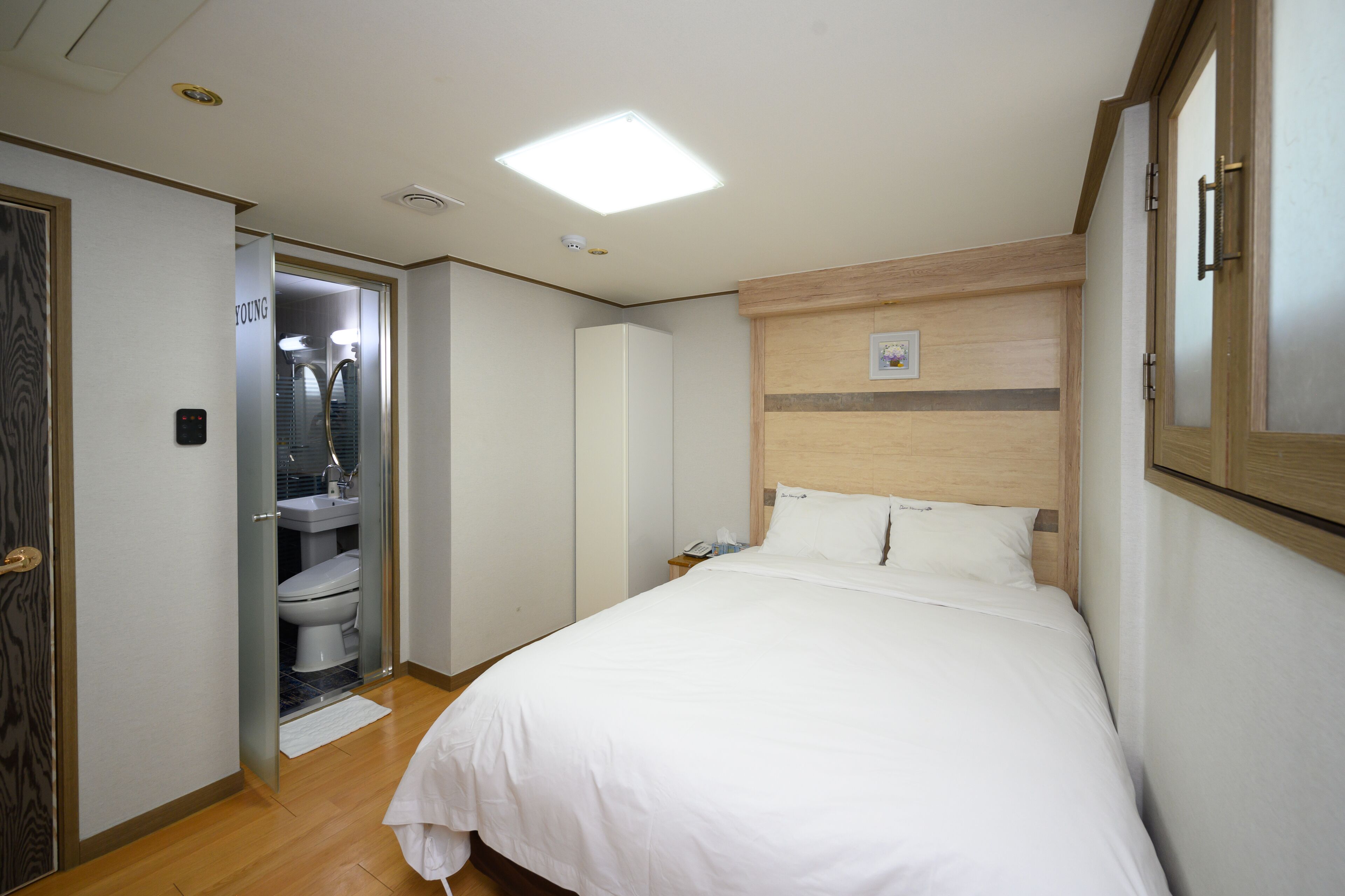Habitación de hotel con una cama, cabecera de madera, mesita de noche y un baño visible a través de una puerta abierta.