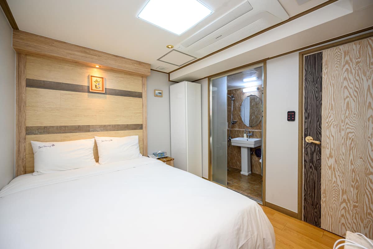 Une chambre d’hôtel comprenant un lit, une table de chevet, un miroir, une salle de bain avec un lavabo et une porte coulissante.