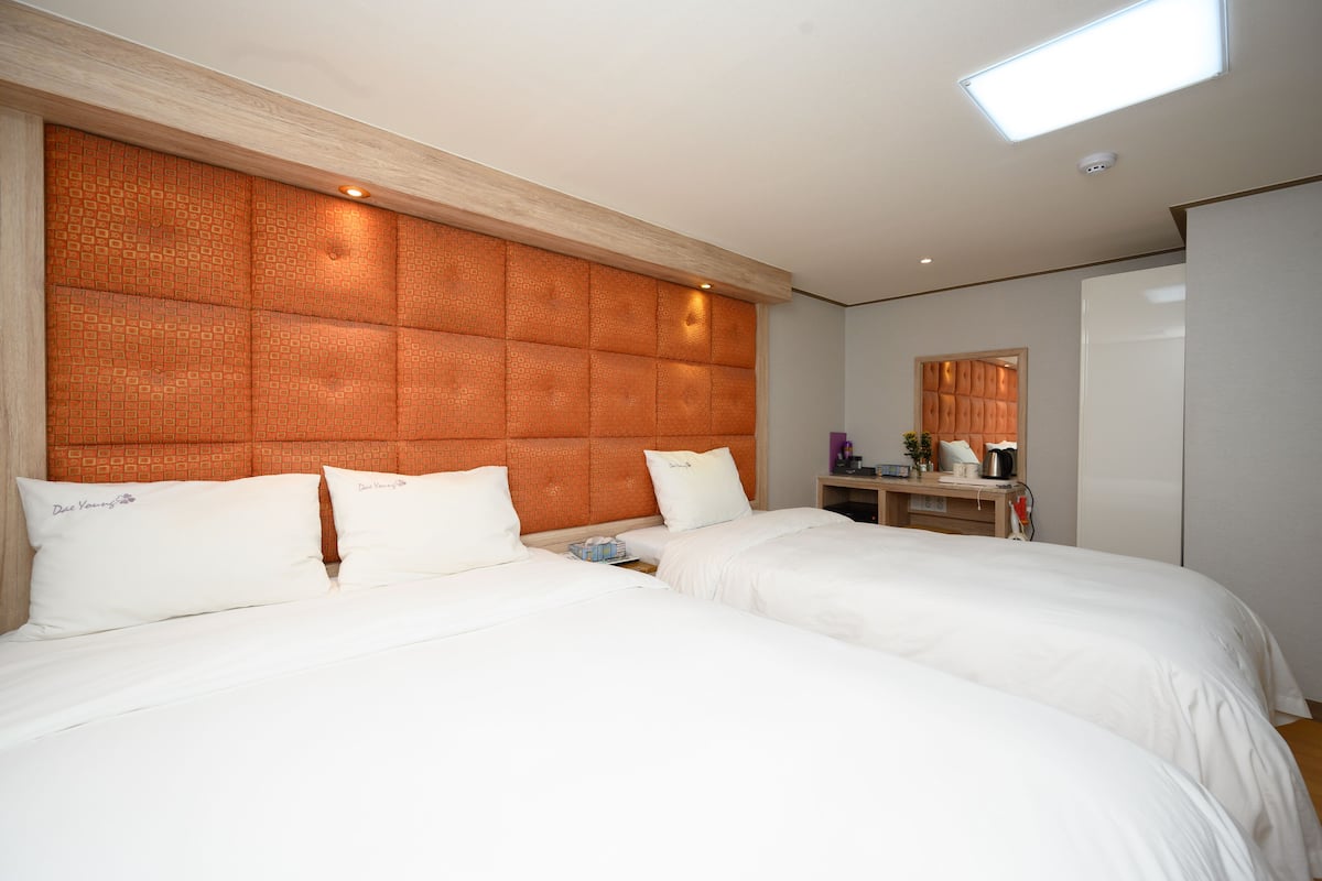 Une chambre d’hôtel avec deux lits, une tête de lit en bois, une table de chevet avec une lampe et un petit bureau avec une chaise.