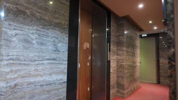 A hallway with a marble wall, a wooden door with a floral design, and a red patterned carpet.