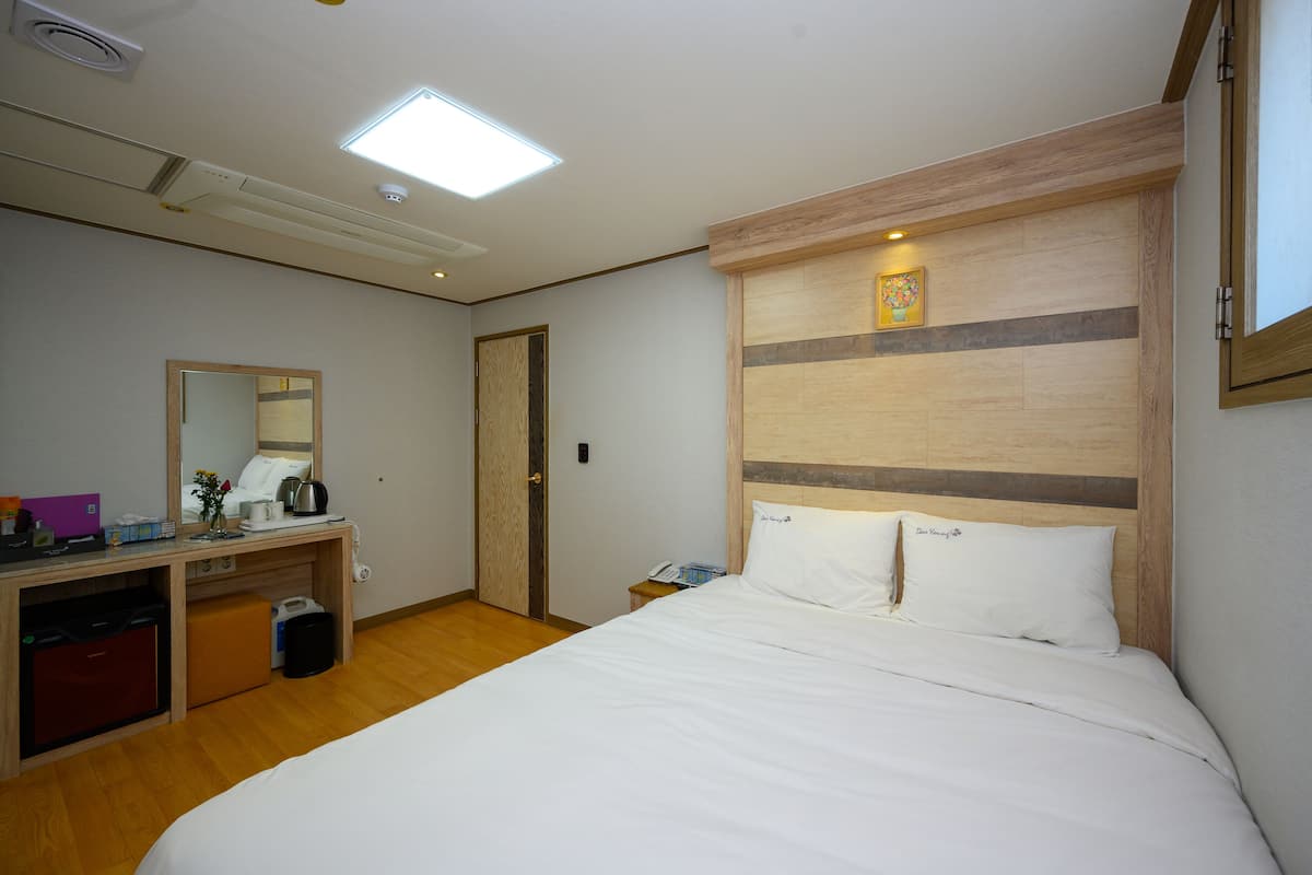 Une chambre d’hôtel équipée d’un lit, d’un bureau, d’un miroir, d’une petite poubelle et d’une table de chevet avec un téléphone.
