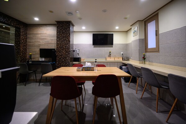A modern dining area with a wooden table, red and grey chairs, a kitchen area with a TV, and a large window. - Daeyoung Hotel Seoul (Seoul)