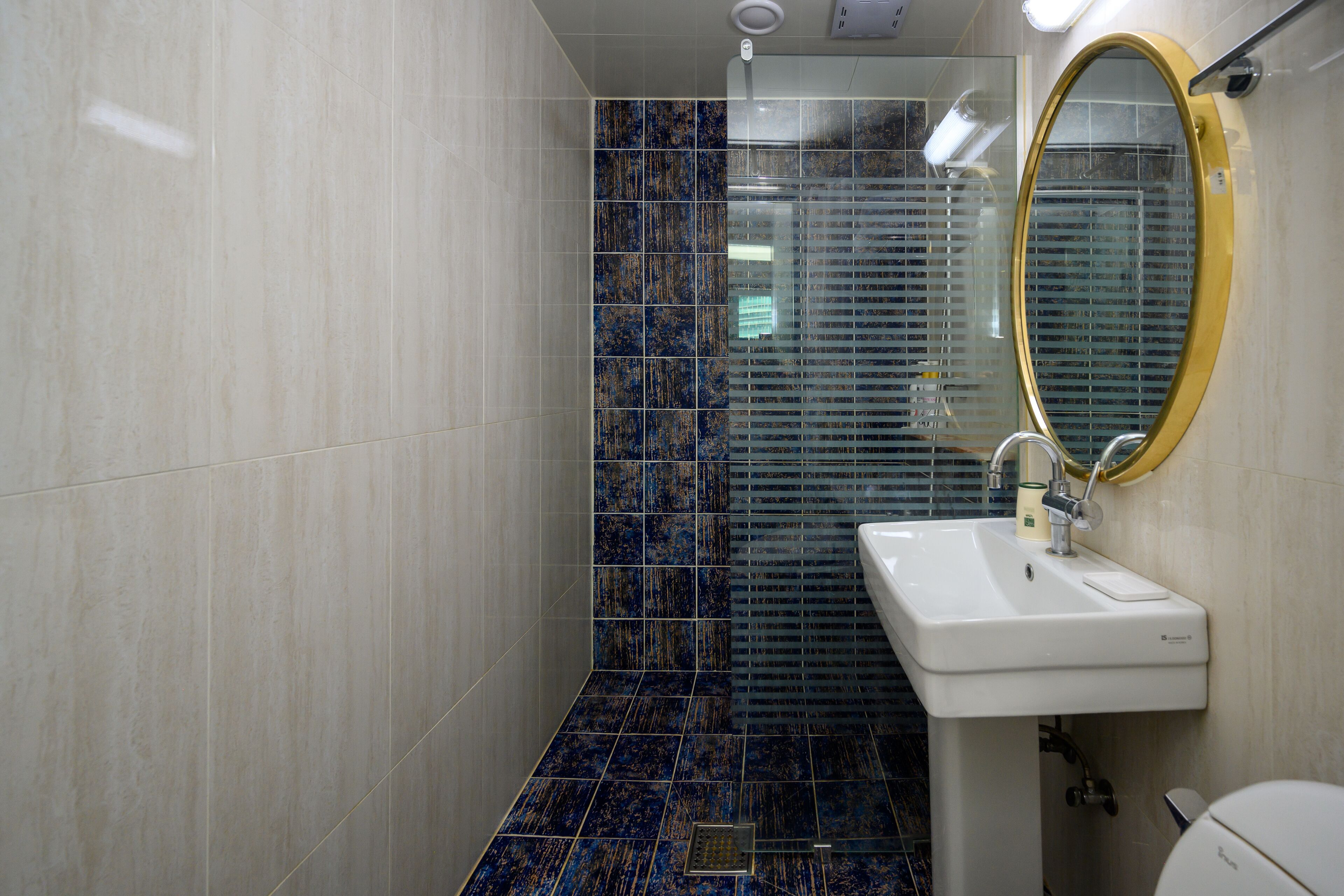 Un baño con lavamanos blanco, espejo y ducha con azulejos azules.