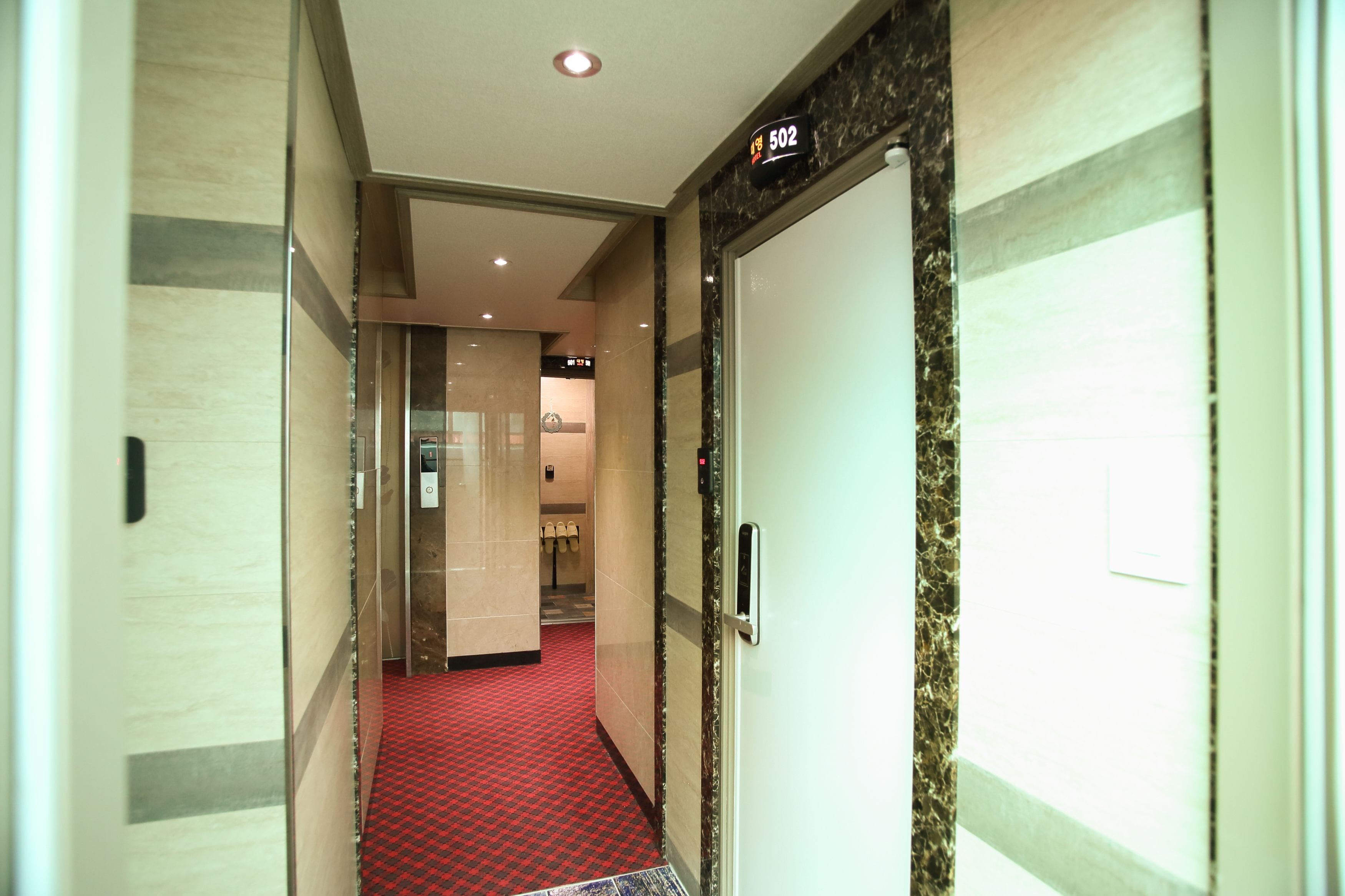 Passadís d'hotel amb una catifa vermella, paret de marbre i una porta amb el símbol de número.