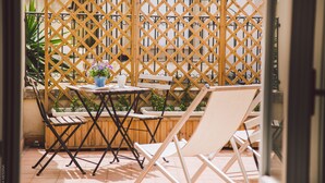 A patio area with a wooden lattice partition, a small table with a potted plant, and two white lounge chairs.
