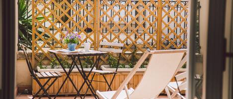 Un patio con un separador de madera celosíaca, una mesita con una planta en maceta y dos sillones blancos.