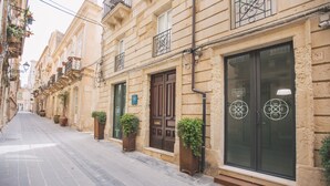 A narrow street lined with historic buildings, featuring large windows and doors, some with decorative ironwork.