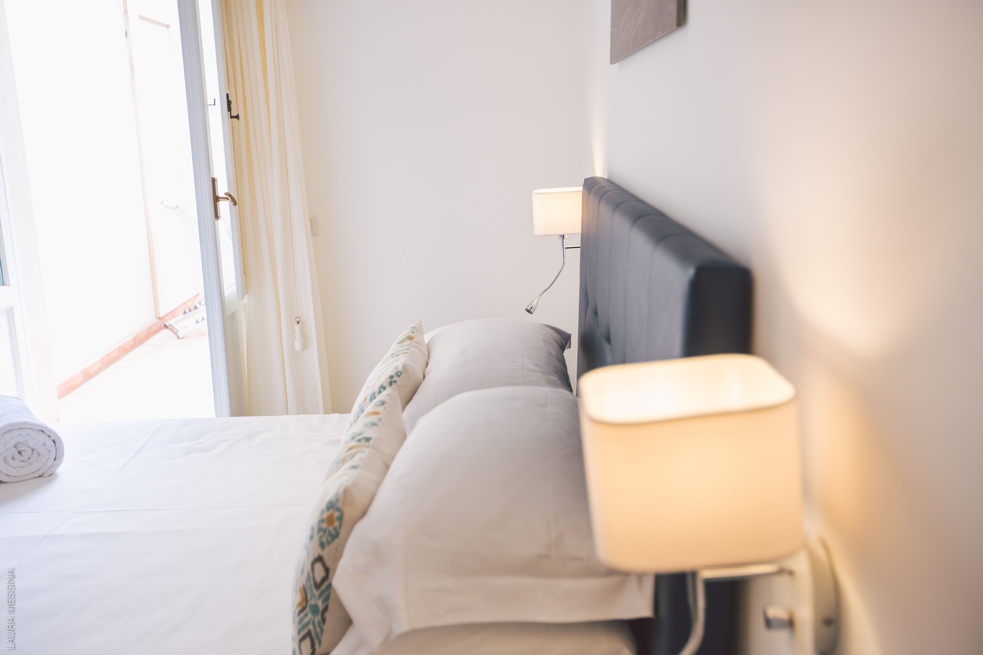 Een hotelkamer met een bed, een bedlampje en een raam met gordijnen.