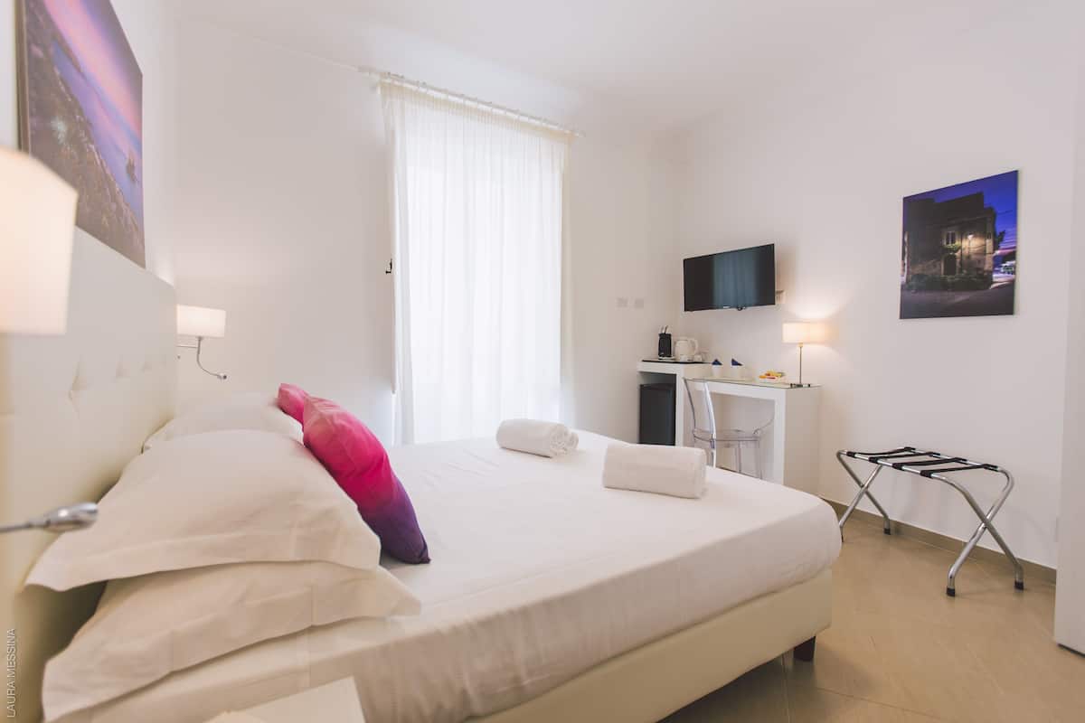Une chambre d’hôtel avec un lit, un bureau, une chaise, une télévision et une fenêtre avec des rideaux.