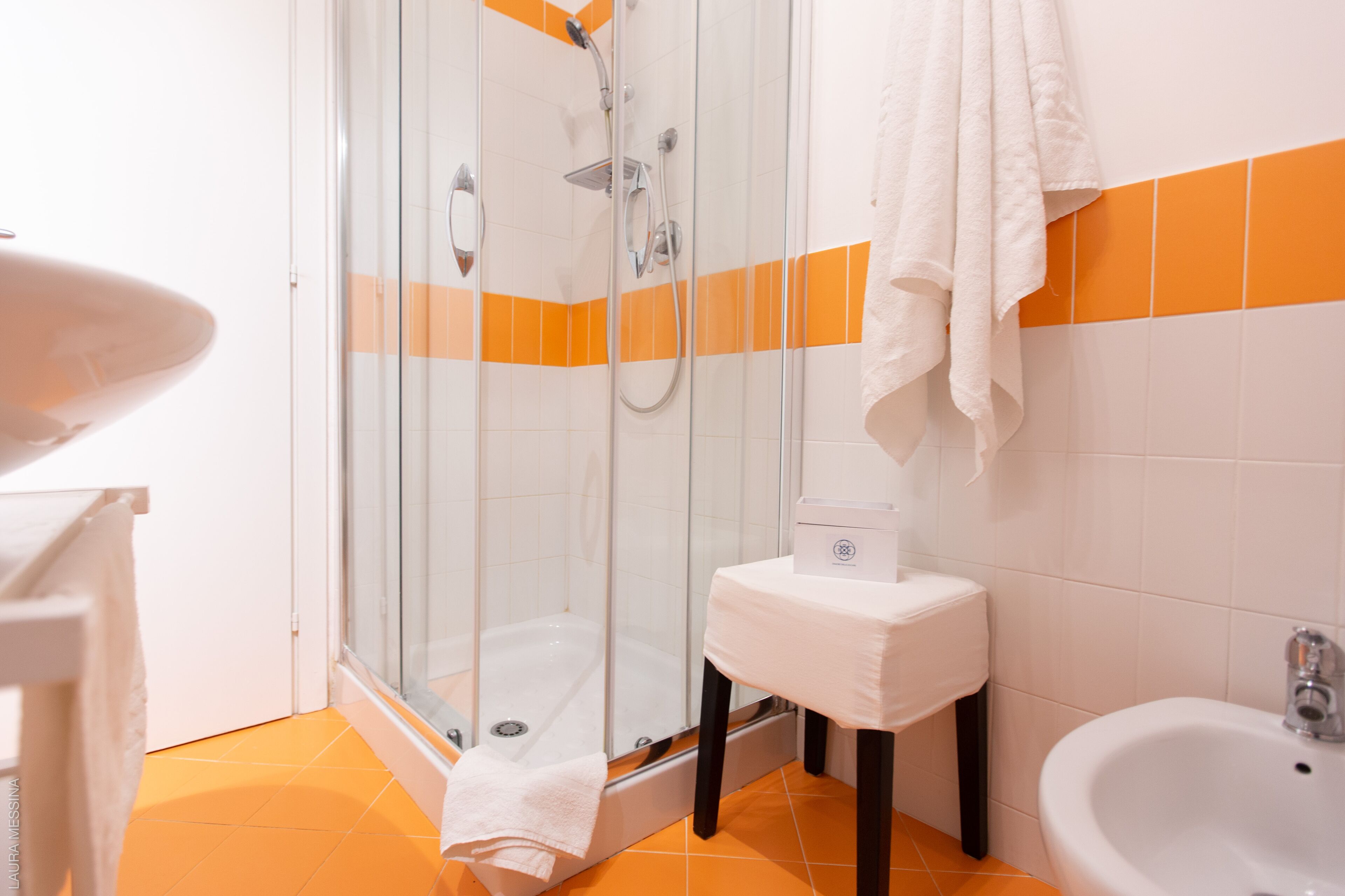 Un baño con ducha envuelta en vidrio, un lavabo blanco y paredes con azulejos naranjas.