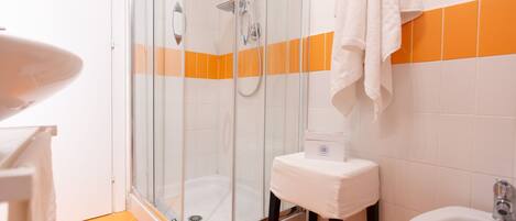 Un baño con ducha envuelta en vidrio, un lavabo blanco y paredes con azulejos naranjas.