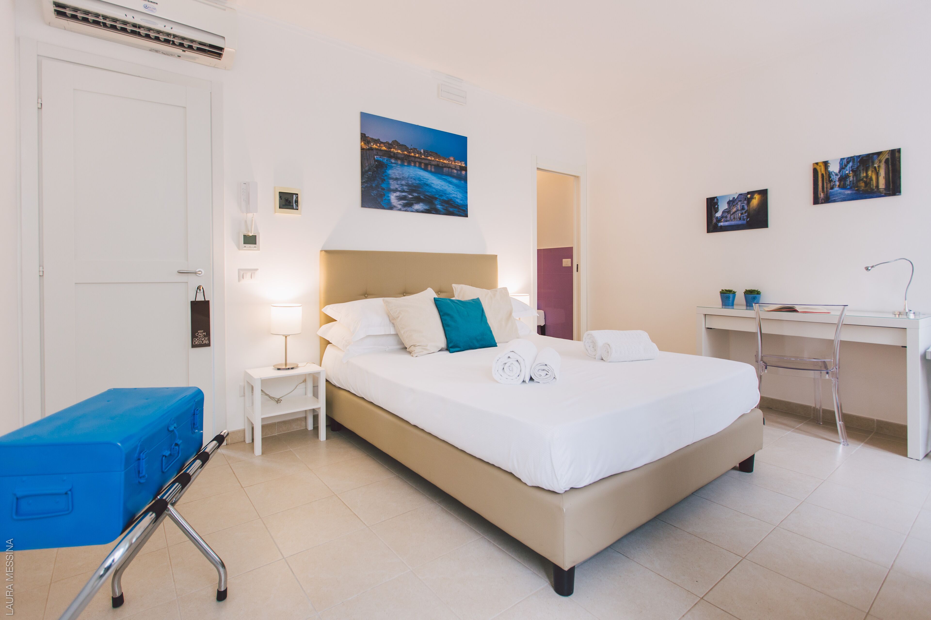 Een hotelkamer met een bed, een bureau, een stoel, een koffer en een nachtkastje met een lamp.