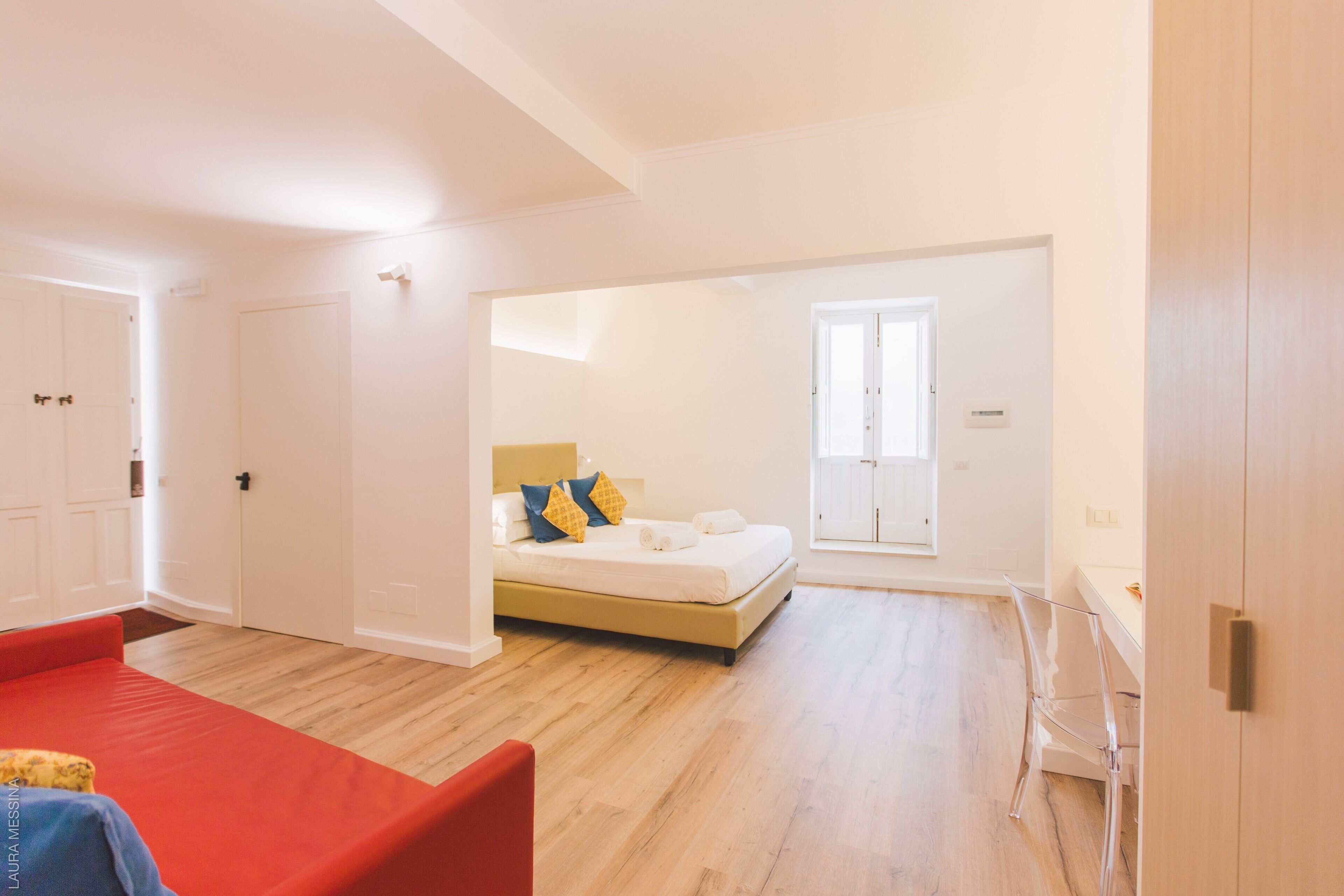 Una habitación amplia con una cama, un sofá rojo y una silla de vidrio transparente.