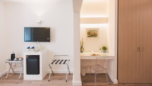 A modern hotel room with a flat-screen TV, a small kitchenette, a desk with a chair, and a wooden wardrobe.
