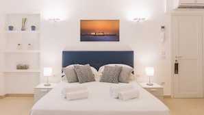 A neatly arranged hotel room with a large bed, two bedside tables with lamps, a wall-mounted air conditioner, and a framed picture above the bed.