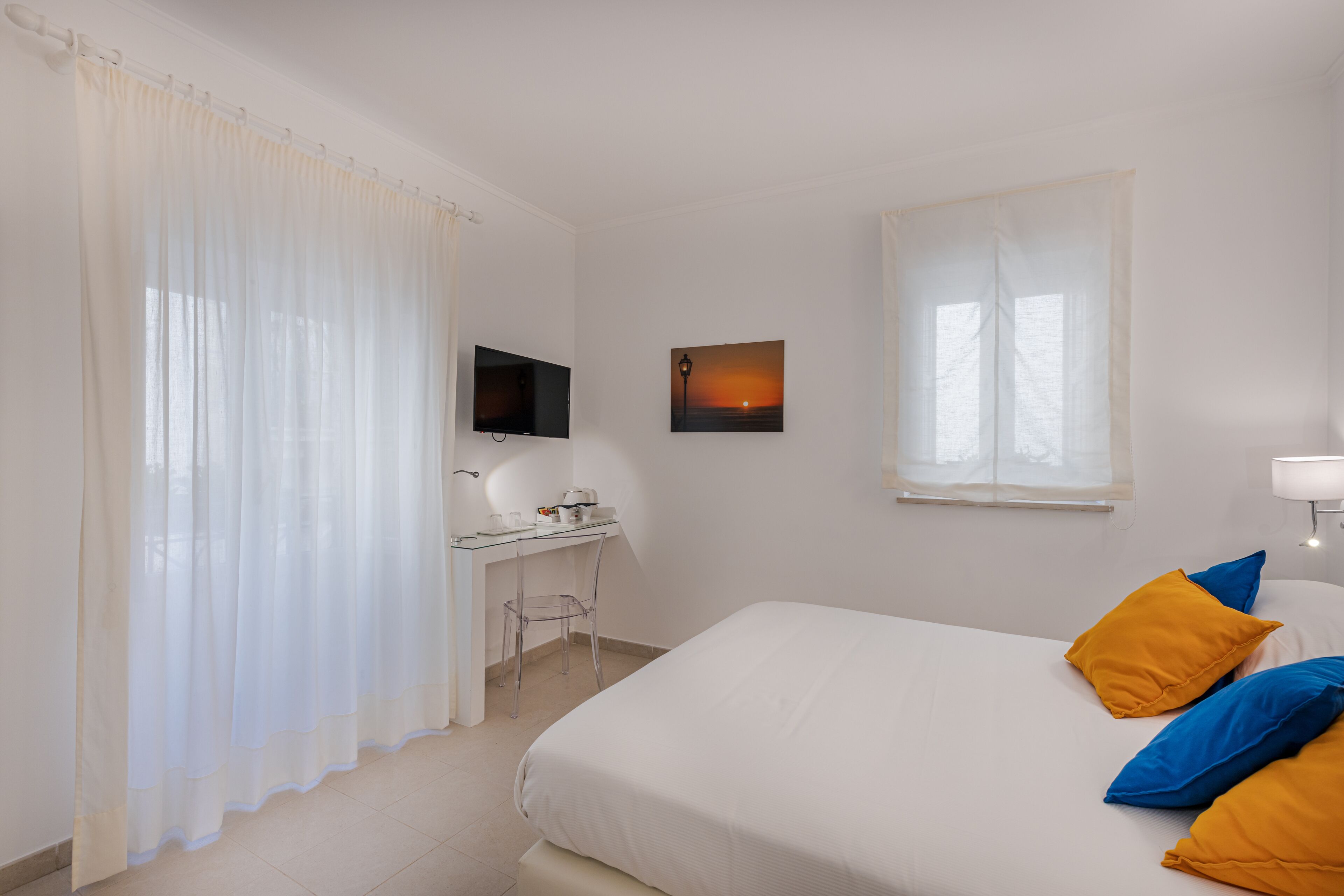A hotel room with a bed, a desk, a chair, a TV, and a window with curtains.