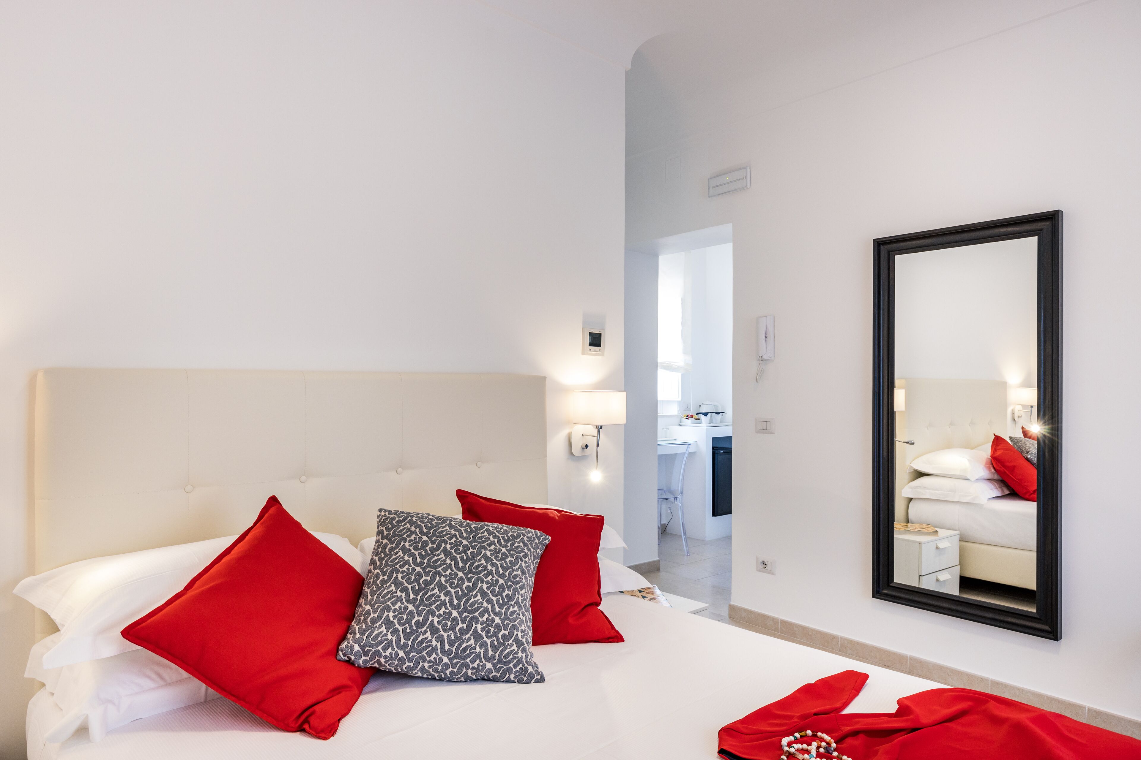 A hotel room with a bed, red and patterned pillows, a large mirror, and a view into the bathroom.