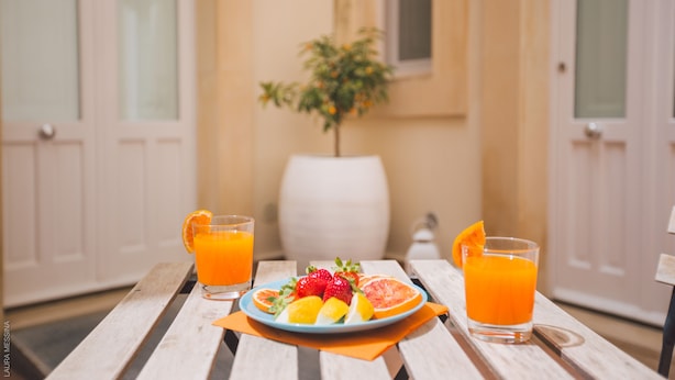 A wooden table with a plate of fruit and two glasses of orange juice.