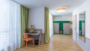 Une chambre moderne équipée d’un bureau, d’une chaise et d’une petite table sur laquelle se trouve un panier de fruits et des verres. On y trouve également une poubelle, un luminaire au plafond et un miroir accroché au mur.