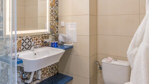 Une salle de bain avec un mur recouvert de carreaux décoratifs, un lavabo blanc, un plan de toilette bleu, des toilettes blanches et une douche en verre.