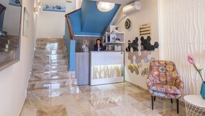 Un hall d’hôtel avec un sol en marbre, un comptoir d’accueil, un fauteuil à motifs et un escalier menant à l’étage supérieur.