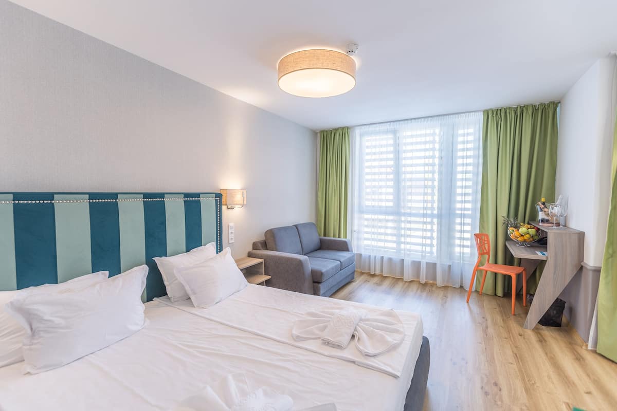 Una habitación de hotel con cama, escritorio, silla y ventana con cortinas.