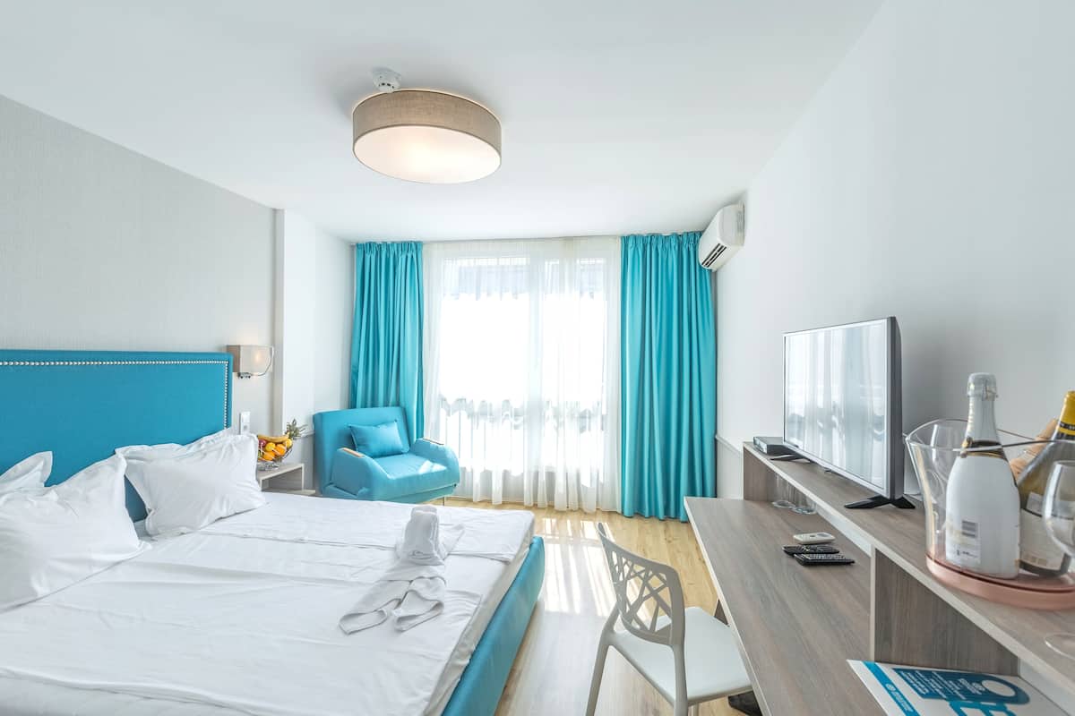 Una habitación de hotel con cama, escritorio, silla, televisor y ventana con cortinas.