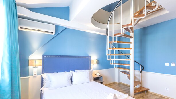 Une chambre à coucher comprenant un lit, une table de chevet, une lampe, un climatiseur et un escalier en colimaçon.