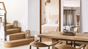Une chambre d’hôtel moderne avec un escalier en bois, un grand lit, une table à manger avec des chaises et un miroir qui reflète la pièce.