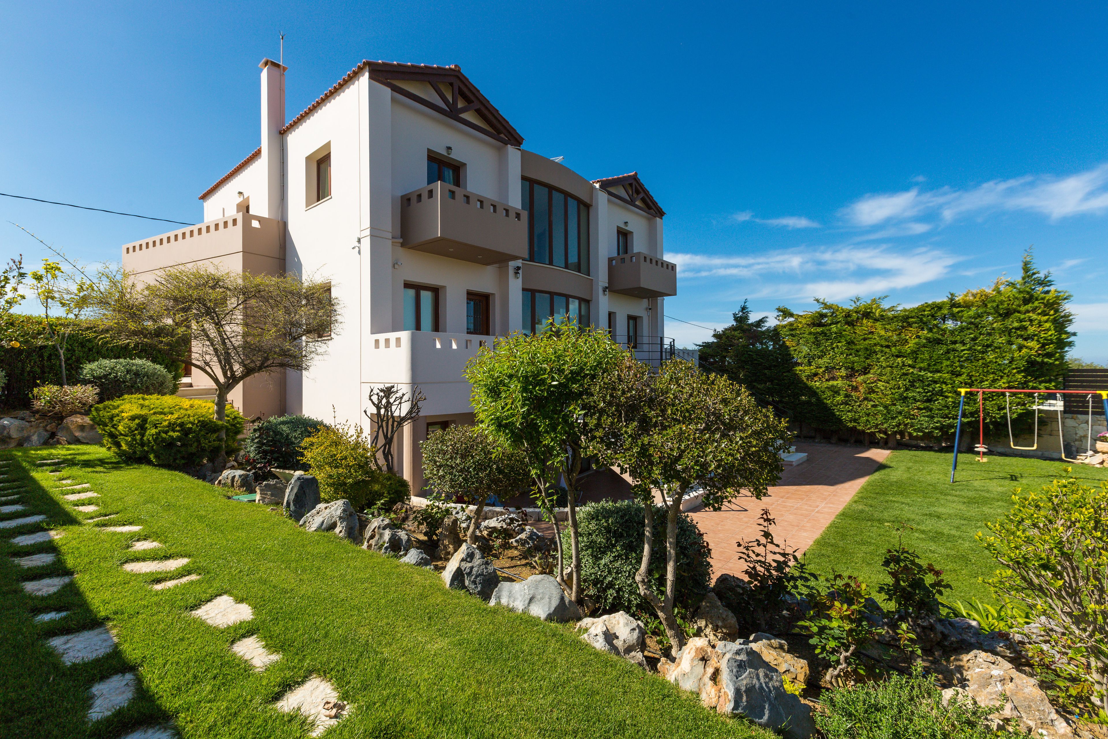 Una casa a due piani con un balcone, un prato curato e un'altalena nel giardino.