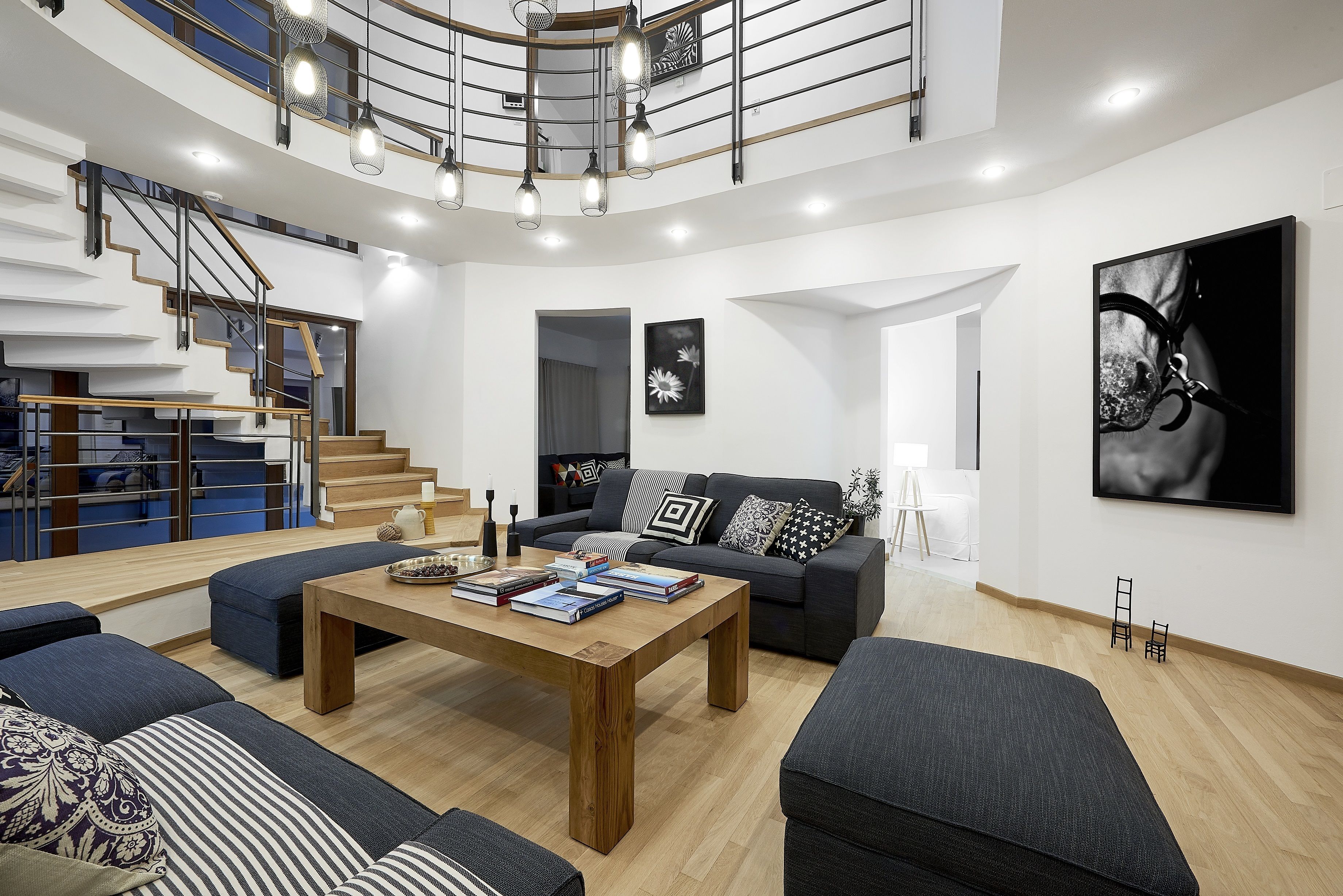 A modern living room with a wooden coffee table, dark sofas, and a staircase with a railing.