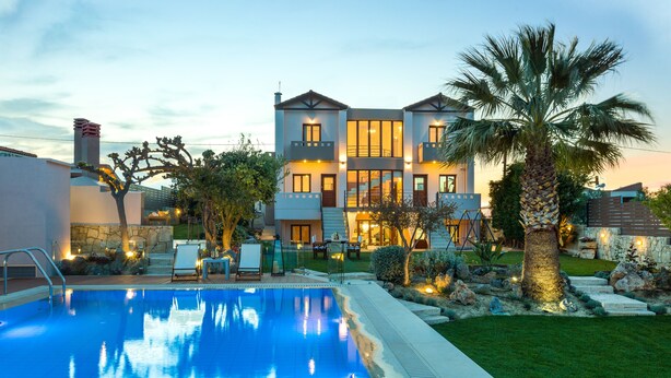 Une maison à deux étages avec une piscine, entourée d’une pelouse bien entretenue et de palmiers.