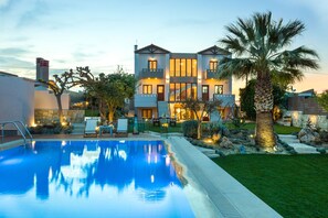Une maison à deux étages avec une piscine, entourée d’une pelouse bien entretenue et de palmiers.