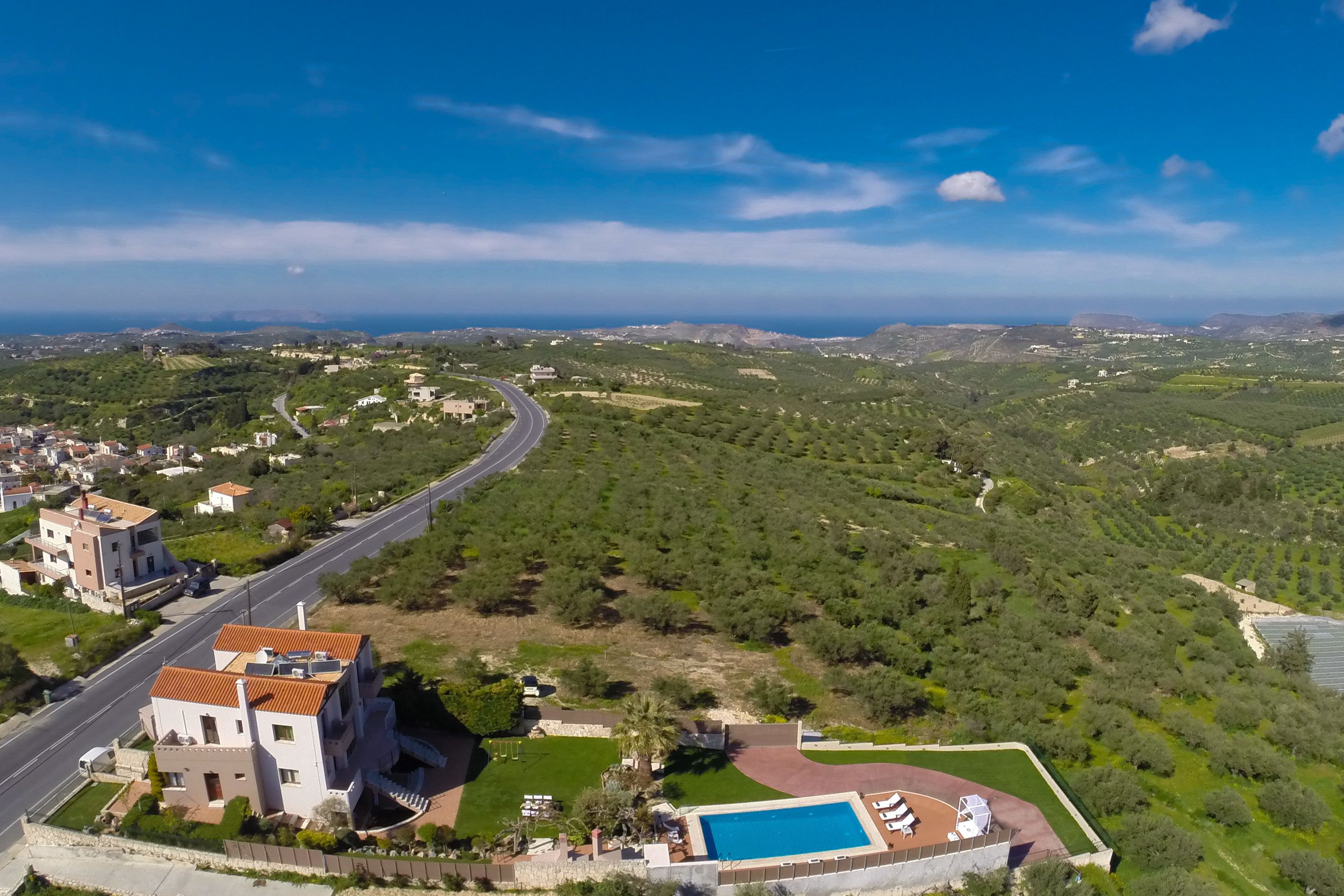 A modern villa with a swimming pool, surrounded by lush greenery and a winding road.