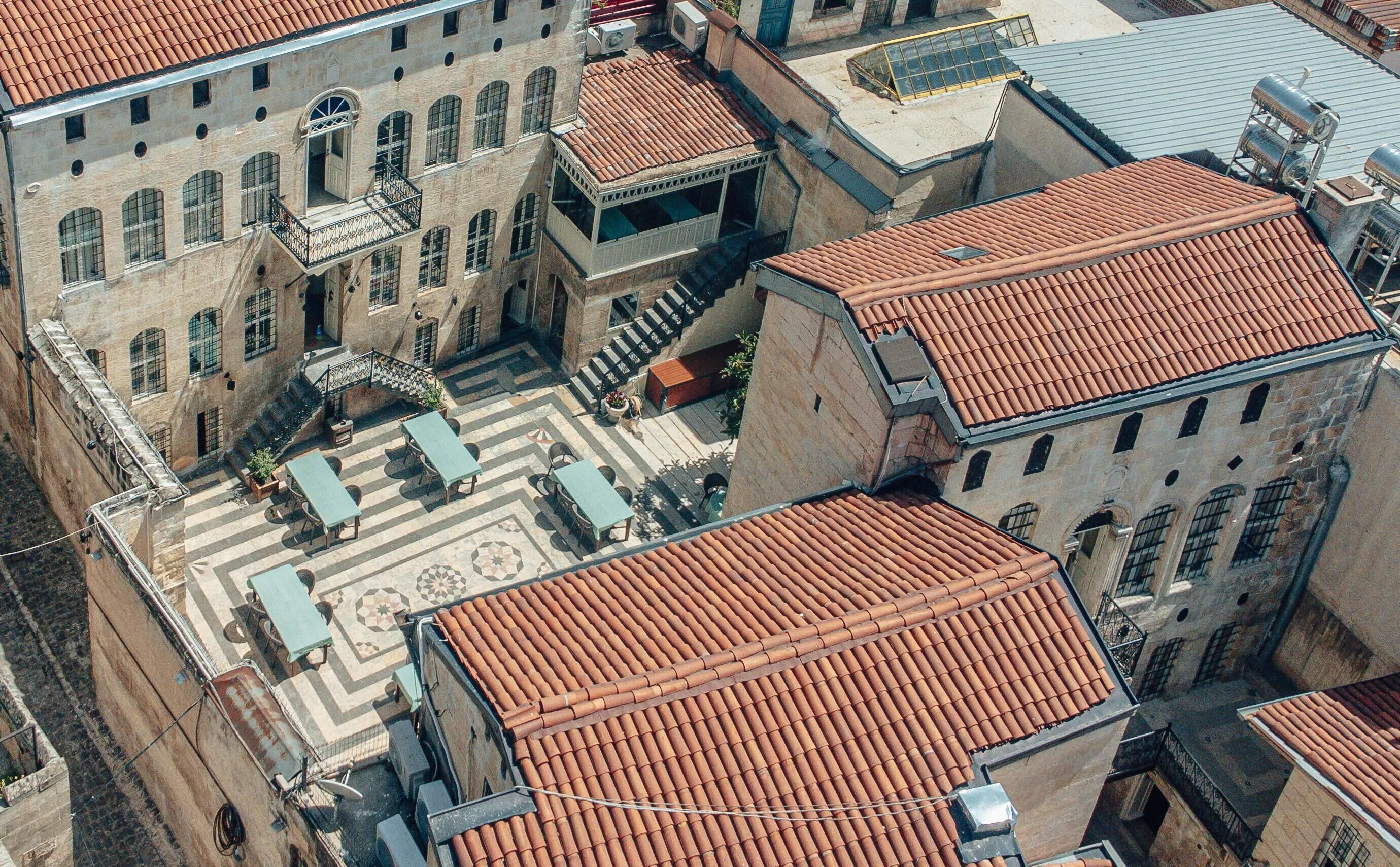 An aerial view of a courtyard with terracotta-tiled roofs, stone buildings, and outdoor seating areas.