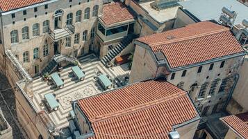 An aerial view of a courtyard with terracotta-tiled roofs, stone buildings, and outdoor seating areas.