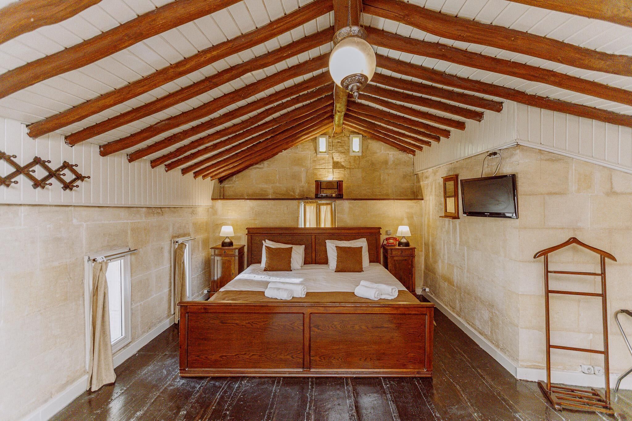 Une chambre spacieuse avec un grand lit en bois, un ventilateur de plafond, une télévision et une échelle en bois.