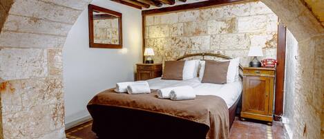Une chambre avec un mur en pierre, un lit en bois, une table de chevet, une lampe et un téléphone.