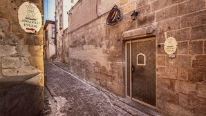 Una estrecha calle empedrada con edificios de piedra, una puerta metálica y dos letreros que dicen 'Anadolu Evleri'.