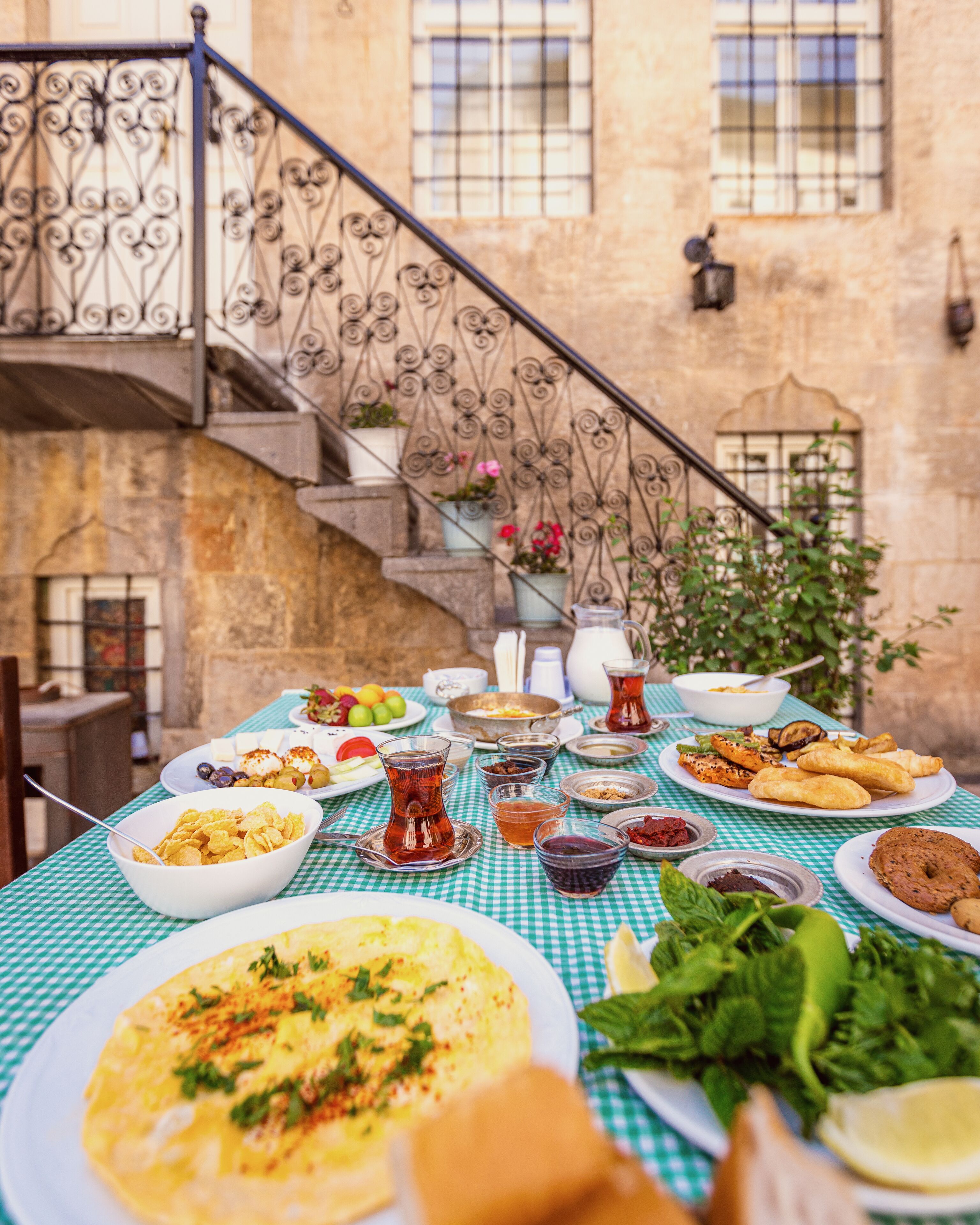 A table set with various dishes and drinks, a staircase, and a stone building in the background.