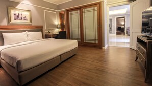 Een hotelkamer met een groot bed, een houten hoofdeinde, een bureau met een lamp, een kledingkast met glazen deuren en een televisie op een dressoir.