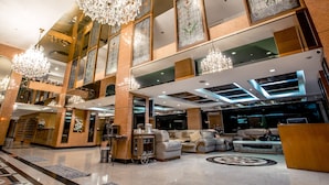 Een ruime lobby met hoge plafonds, grote kroonluchters en een zithoek met banken en een salontafel.
